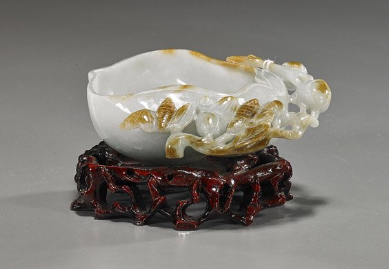 Chinese Carved Jade Brushwasher: Chinese Carved Jade Brushwasher Chinese carved Jade brushwasher; of somewhat pear form and with openwork peaches and bats at the rim; light green color with russet suffusions; L: 4", wood stand