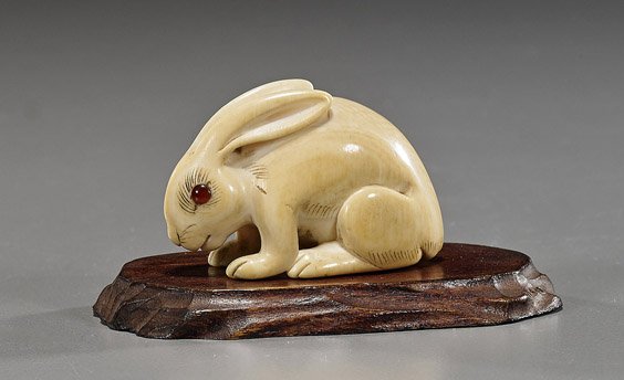 Old Carved Ivory Netsuke: Rabbit: Old Carved Ivory Netsuke: Rabbit Early 20th Century carved ivory netsuke; of a rabbit, inlaid eyes, fine patina, wood stand