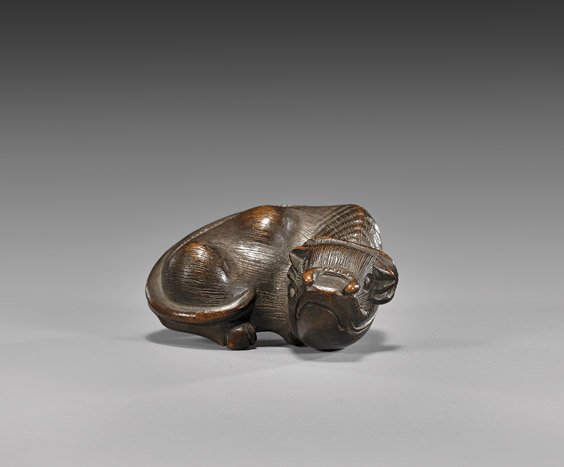 ANTIQUE WOOD NETSUKE: Water Buffalo: 木製根付 ANTIQUE WOOD NETSUKE: Water Buffalo Finely detailed, antique carved wood netsuke: of a recumbent water buffalo; the wood showing good patina; unsigned; early 19th Cent
