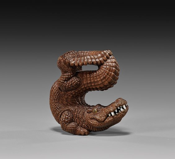 CARVED WOOD NETSUKE: Alligator: 木製根付 短吻鱷 CARVED WOOD NETSUKE: Alligator Elaborately carved wood netsuke by Kozan; of an alligator balancing on its two front legs and with its tail twi