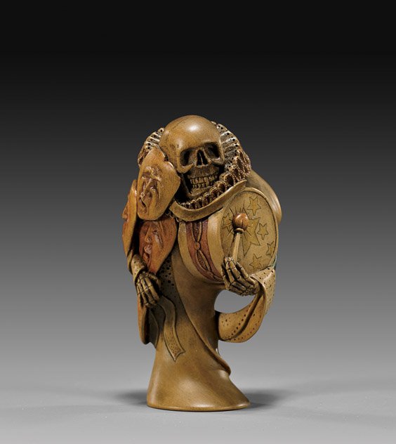 CARVED WOOD NETSUKE: Skeleton: 木製根付 骷髏 CARVED WOOD NETSUKE: Skeleton Large carved and lacquered wood netsuke by David Carlin; of a skeleton in old English dress with a ruff collar, holding 