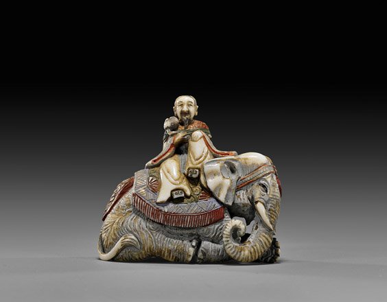 ANTIQUE CARVED IVORY NETSUKE: Elephant: 象牙根付 ANTIQUE CARVED IVORY NETSUKE: Elephant Antique carved and polychromed ivory netsuke; of a nobleman seated atop an ornately caparisoned recumbent elephant, signed in ov