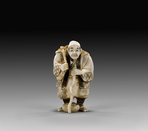 CARVED IVORY NETSUKE: Walking Man: 象牙根付 CARVED IVORY NETSUKE: Walking Man Early 20th Century, carved ivory netsuke; of a man with gnarled walking stick, and with a large bundle of vegetables thrown over his 