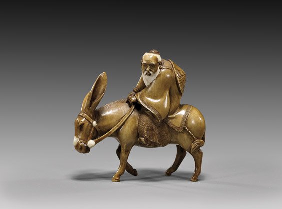 CARVED IVORY OKIMONO: Sage & Donkey: 象牙根付 CARVED IVORY OKIMONO: Sage & Donkey Finely carved and stained ivory netsuke-sized okimono; of a bearded sage riding on a donkey, signed; wood box; Provenance: The Esta