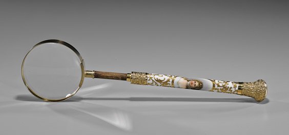 ANTIQUE CONTINENTAL MAGNIFYING GLASS: 歐陸風格放大鏡 ANTIQUE CONTINENTAL MAGNIFYING GLASS Antique Continental magnifying glass; the handle mounted in repoussé gilt metal, with scrolling gilt deco
