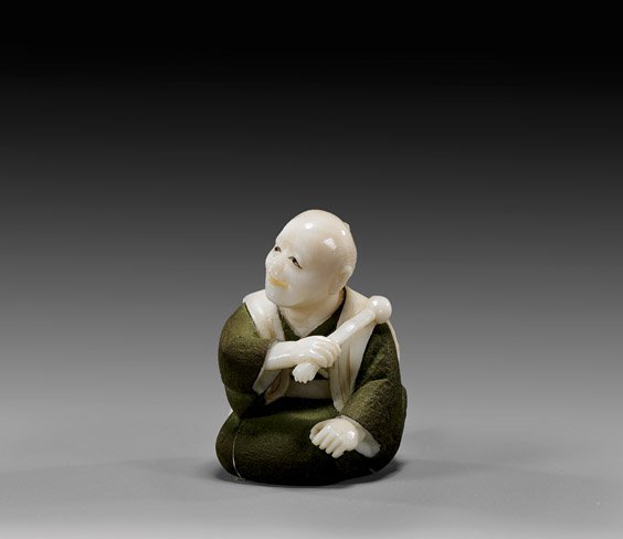 LACQUERED IVORY NETSUKE: Seated Man: LACQUERED IVORY NETSUKE: Seated Man Lacquered and carved ivory netsuke by Hodo Sekizawa; of a seated man in green lacquered robes, holding a massage stick over one shoulder, signed in square gilt rese