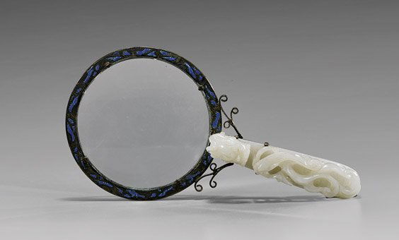 ANTIQUE JADE-SET MAGNIFYING GLASS: ANTIQUE JADE-SET MAGNIFYING GLASSAntique magnifying glass, with enameled frame, Circa 1900; the handle set with an antique openwork carved white jade dragon belt buckle, the buckle 19th Century or ear