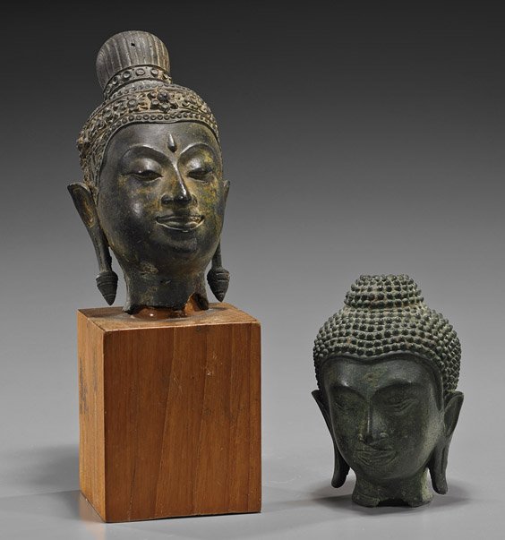Two Antique Southeast Asian Bronze Heads: Two Antique Southeast Asian Bronze Heads Two early Southeast Asian, probably Thai, bronze Buddhist heads: one finely detailed with large pendant earrings and floral headdress, 17th Century, wood stand