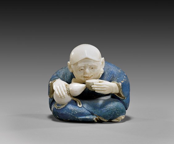 POLYCHROMED IVORY NETSUKE: Actor: POLYCHROMED IVORY NETSUKE: Actor Finely carved and polychromed, figural ivory netsuke; of a seated actor drinking sake, an Okame mask hung from his neck to the back, with a pipe and tobacco pouch, sig