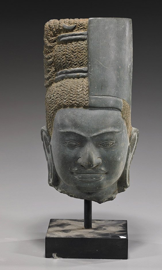 Unusual Cambodian-Style Carved Stone Head: Unusual Cambodian-Style Carved Stone Head Unusual Cambodian-style carved stone head; with serene expression to the face and elongated earlobes, wearing a tall bisected hat/headdress; H: 11 1/2", wood 