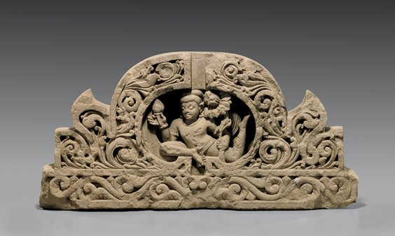 ANTIQUE GANDHARAN BUDDHIST SCHIST LINTEL: ANTIQUE GANDHARAN BUDDHIST SCHIST LINTEL Antique Gandharan carved schist lintel; with Buddhist figural design, centering an agile deity holding lotus blossom and bud, encircled by a foliate border, an