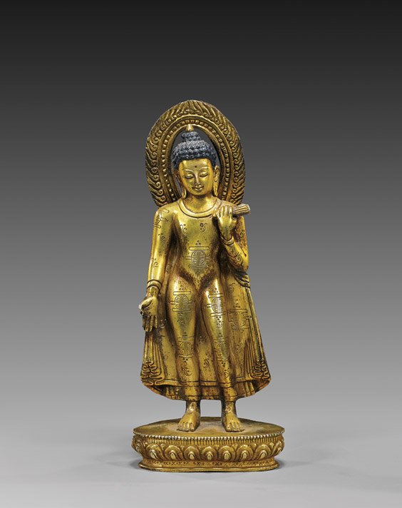 TIBETAN OR NEPALESE GILT BRONZE BUDDHA: TIBETAN OR NEPALESE GILT BRONZE BUDDHA Tibetan or Nepalese gilt bronze standing figure of Buddha; holding a folded fan in his left hand, his right hand in mudra, wearing an unusual drapery with Shou m