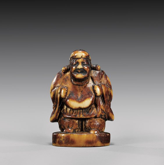 ANTIQUE CARVED IVORY NETSUKE/SEAL: Deity: 象牙根付 ANTIQUE CARVED IVORY NETSUKE/SEAL: Deity Antique and finely patinated, carved ivory netsuke/seal; of a standing deity, atop an oval seal base, early 19th Century