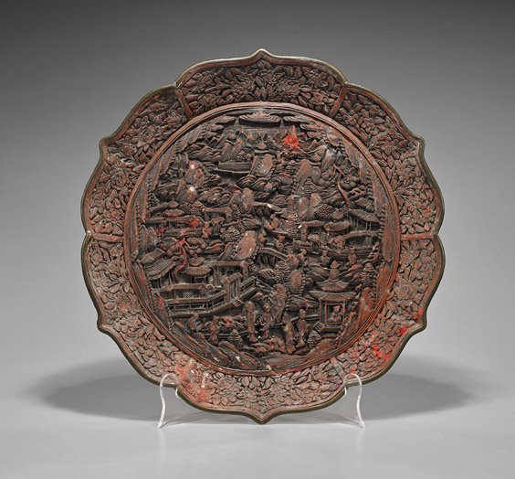 Chinese Cinnabar Lacquered Foliate Dish: Chinese Cinnabar Lacquered Foliate Dish Chinese cinnabar lacquered dish; of circular form with foliate edges, depicting a village scene with numerous figures outside walking along the paths, Buddhist 