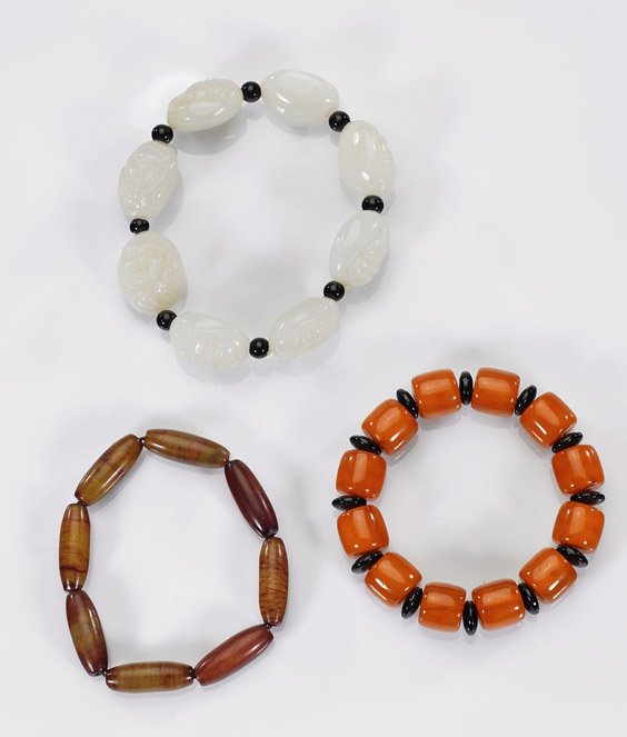 Three Chinese Bead Bracelets: Three Chinese Bead BraceletsGroup of three Chinese bead bracelets: carved whitish-celadon with various forms of Budai, onyx spacers; tubular agate with varying shades of red; together with amber-like