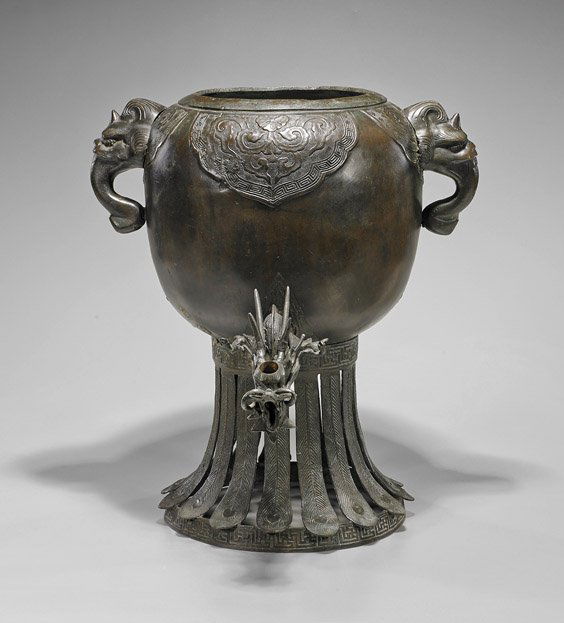 Large Old Japanese Bronze Wine Vessel: Large Old Japanese Bronze Wine VesselLarge old Japanese bronze wine vessel; of rounded body suspended above circular base with "feather" supports, mask handles and dragon spout attachments, foliate ac