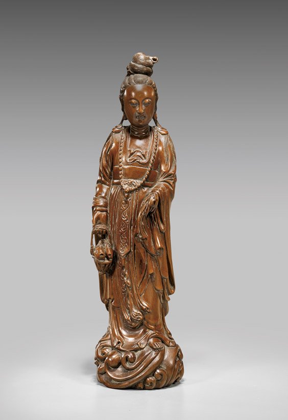 CARVED BOXWOOD GUANYIN FIGURE: 木雕觀音立像 CARVED BOXWOOD GUANYIN FIGURETall Chinese carved boxwood figure; of Guanyin standing in layered robes and carrying a basket of fish, upon a bulbous bas