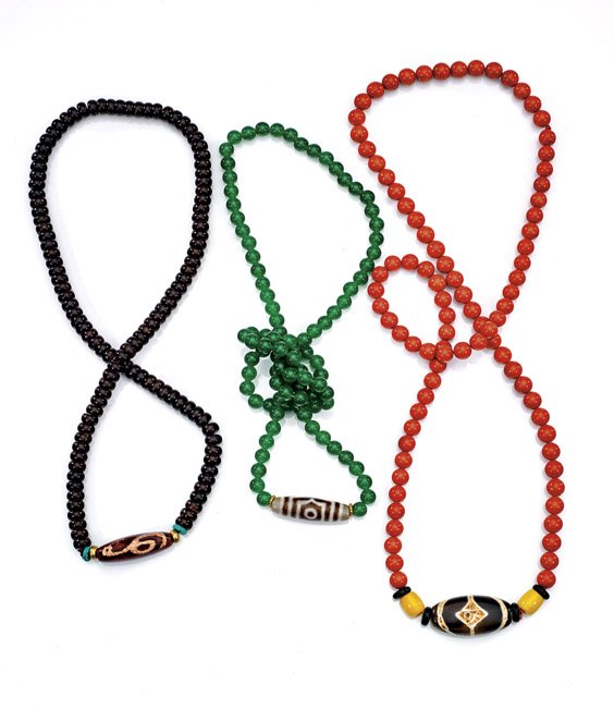 THREE PRAYER BEAD NECKLACES: THREE PRAYER BEAD NECKLACES Three Buddhist prayer bead necklaces: round green quartzite with dzi bead; round coral with two yellow glass beads flanking a flattened dzi bead; and coconut roundels with 