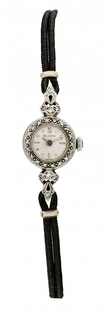 BULOVA 14K GOLD & DIAMOND WATCH: BULOVA 14K GOLD & DIAMOND WATCH 14K white gold ladies' diamond Bulova watch; the delicate piece with small round face, textrued radiating dial, framed by a diamond-set bezel, with foliate details to e
