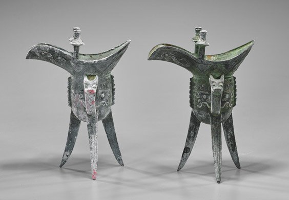 Two Archaistic Chinese Bronze Jue Cups: Two Archaistic Chinese Bronze Jue Cups Two archaistic Chinese bronze tripod jue wine cup; single dragon head handle with a taotie mask body, two posts at either side of the trough-form spout; set upon