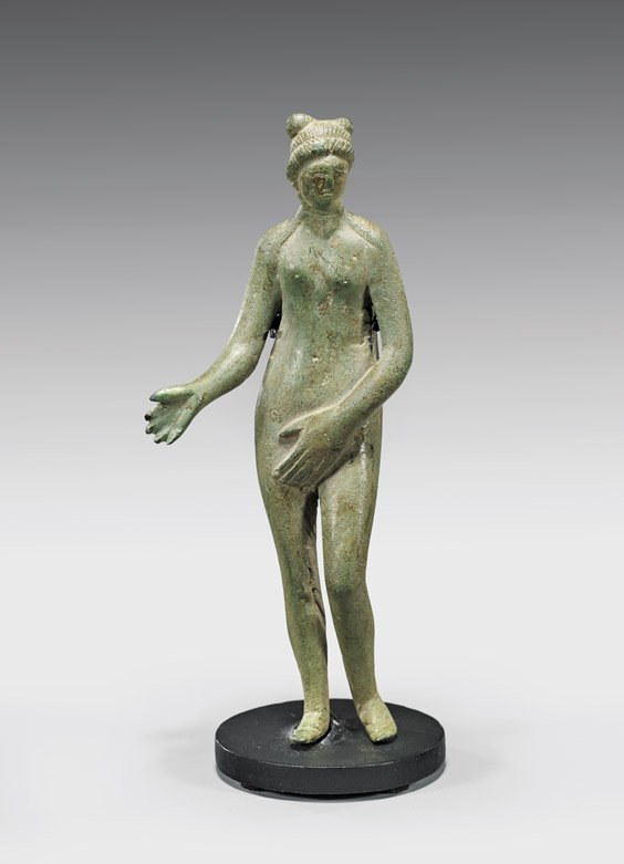 ROMAN BRONZE VENUS: ROMAN BRONZE VENUS Roman bronze nude figure of Venus; depicted in her modest form, with left hand over her genitalia and right hand extended; her hair framing her face and forming two coils at the bac