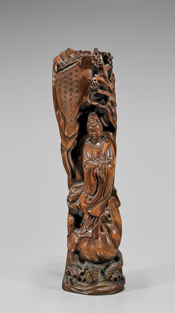 TALL CARVED WOOD GUANYIN: TALL CARVED WOOD GUANYINChinese carved and stained wood figure; of Guanyin standing in flowing robes with her eyes closed, on lotus base upon waves, with rockery and scrolling clouds behind her, an in