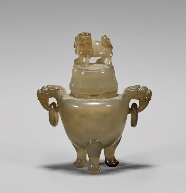 ANTIQUE CARVED AGATE TRIPOD CENSER: Antique Chinese carved agate tripod censer; the well-hollowed translucent body with two lion-headed handles pending loose rings; the tall cover surmounted with lion finial; all set atop three sinuous