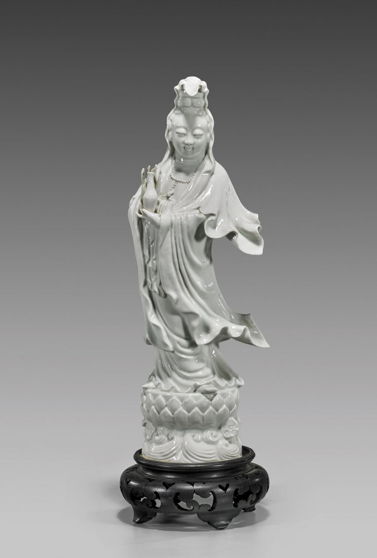 OLD BLANC DE CHINESE PORCELAIN GUANYIN: Old Chinese blanc de chine porcelain figure of Guanyin; standing in flowing robes, and holding up her bottle of tears; atop lotus pedestal on a base of waves; early 20th Century; Provenance: From the 