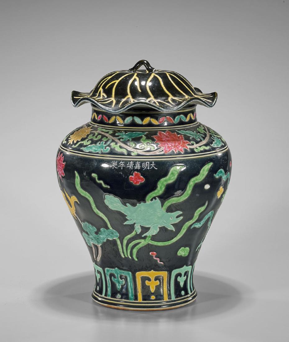 Famille Noire Porcelain Covered Jar: Chinese Famille Noire porcelain baluster jar; the cover moulded and incised in imitation of a lotus pad; the body with incised and painted design of fish swimming amid pond flora; six-character Jiajin