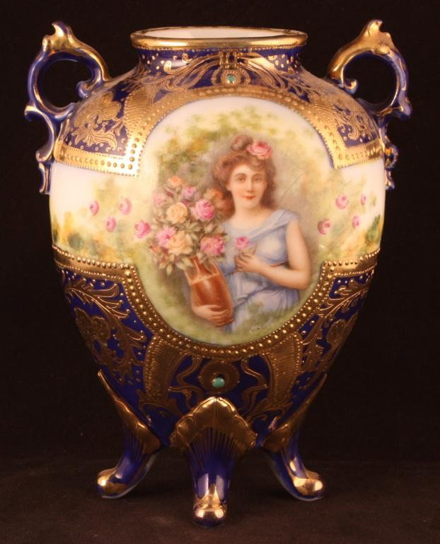 NIPPON Cobalt Portrait Vase on Four Feet: 7 1/2" tall. Woman holding vase filled with flowers. Jeweled at top and bottom of portrait. Nice gold scroll decor throughout. Mark 52. Excellent condition with gold loss to handles and top of shoulde