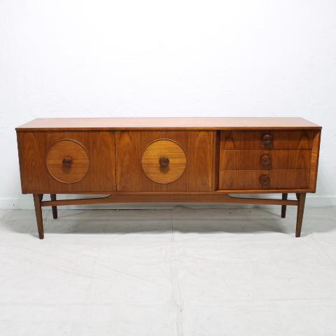 Teak Mid Century Sideboard: This British Mid Century Sideboard is Danish Modern in Style. Teak Veneer, features round handles, three drawers and two drawers with circular panels & an open stretcher base.