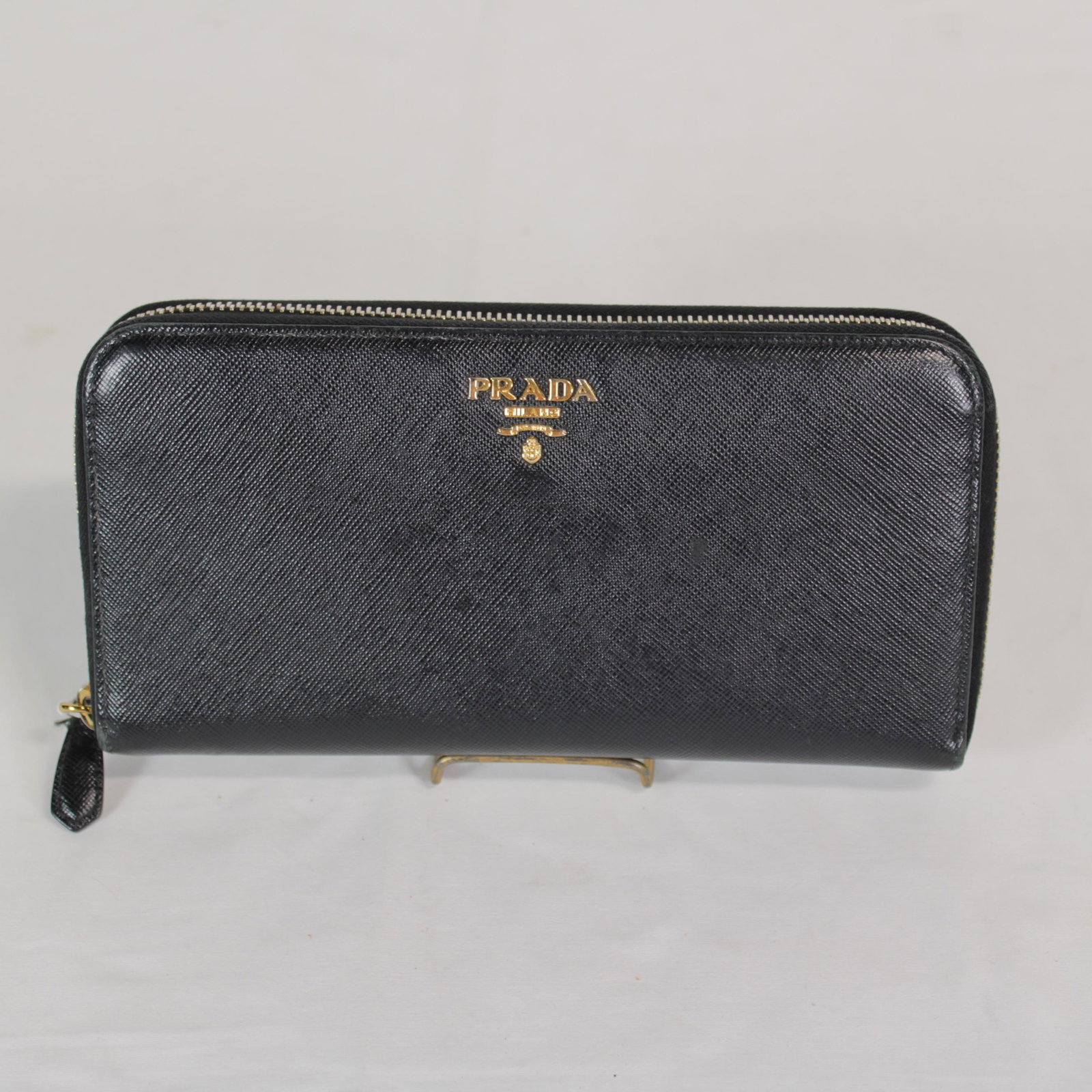 Prada Saffiano Zip Wallet in Saffiano Leather: Genuine Pre-Owned Prada Saffiano Zip Wallet in Black Saffiano Leather in AB condition. Date Code is N/A. Measurements: 20*10*3cm (Length * Height * Width). This lot includes a certificate of authentic