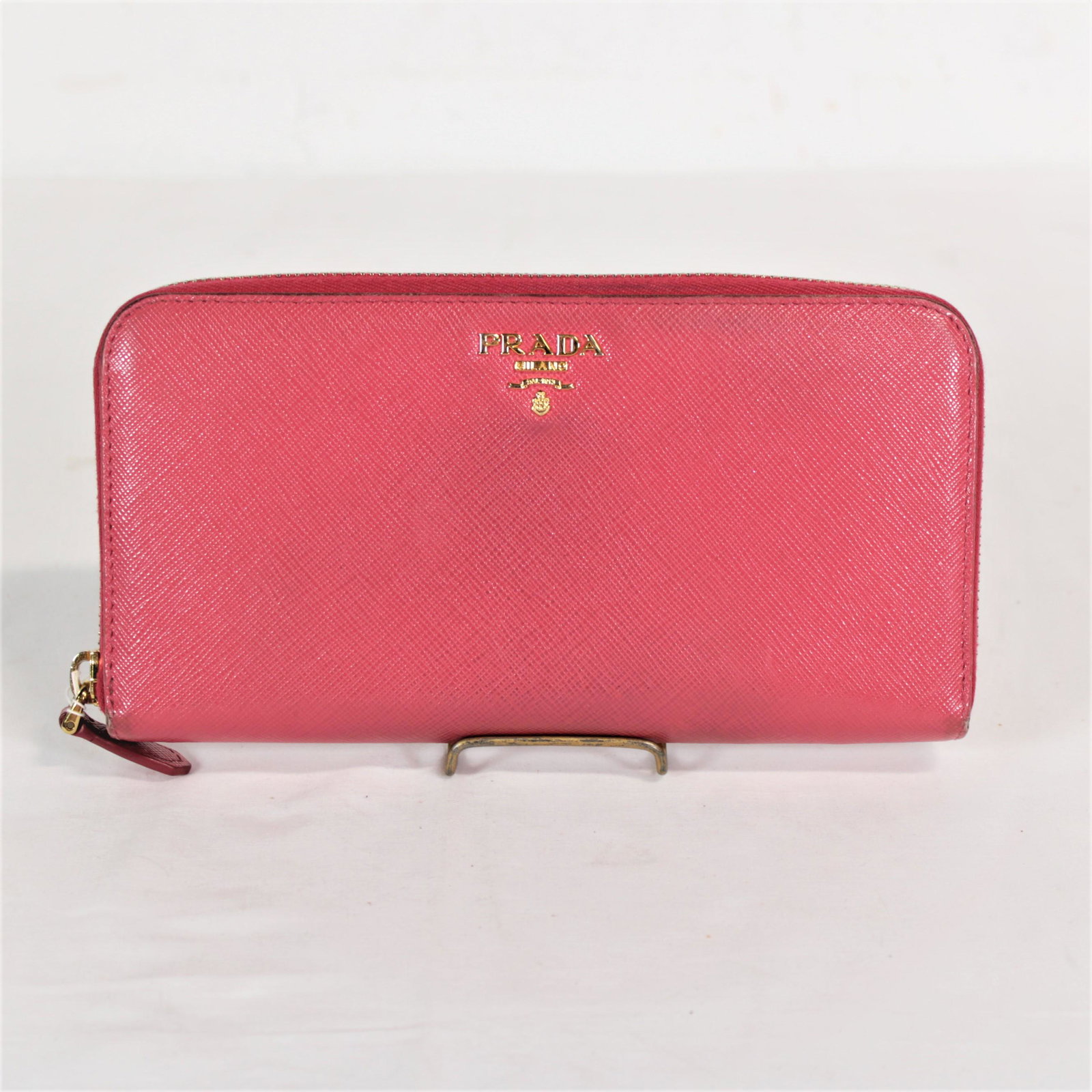 Prada Zip-Around Wallet in Saffiano Leather: Genuine Pre-Owned Prada Zip-Around Wallet in Pink Saffiano Leather in AB condition. Date Code is N/A. Measurements: 20*10*2cm (Length * Height * Width). This lot includes a certificate of authenticity