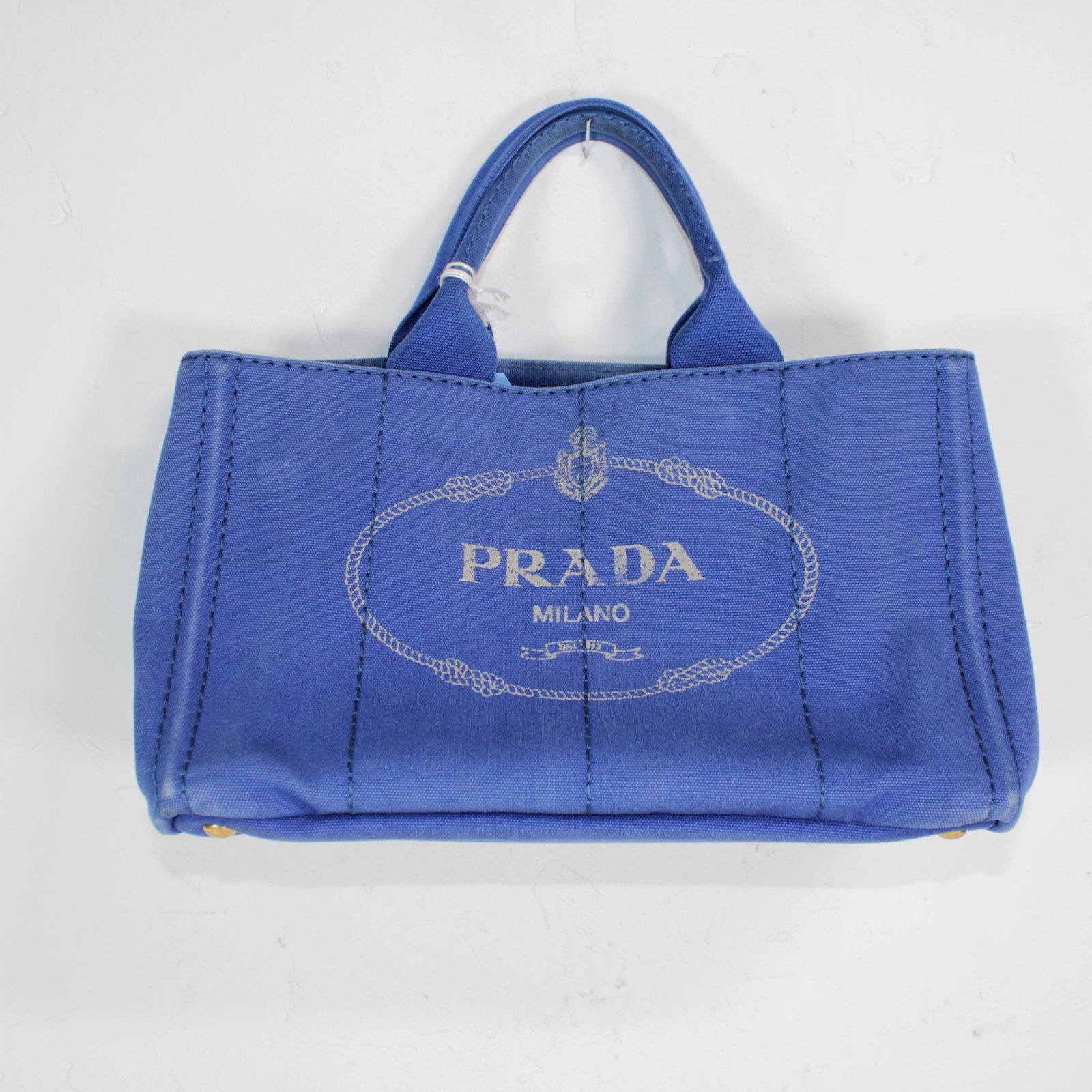 Prada Canapa Tote in Canvas: Genuine Pre-Owned Prada Canapa Tote in Blue Canvas in AB condition. Date Code is N/A This lot includes Strap. Measurements: 36*21*21cm (Length * Height * Width). This lot includes a certificate of aut