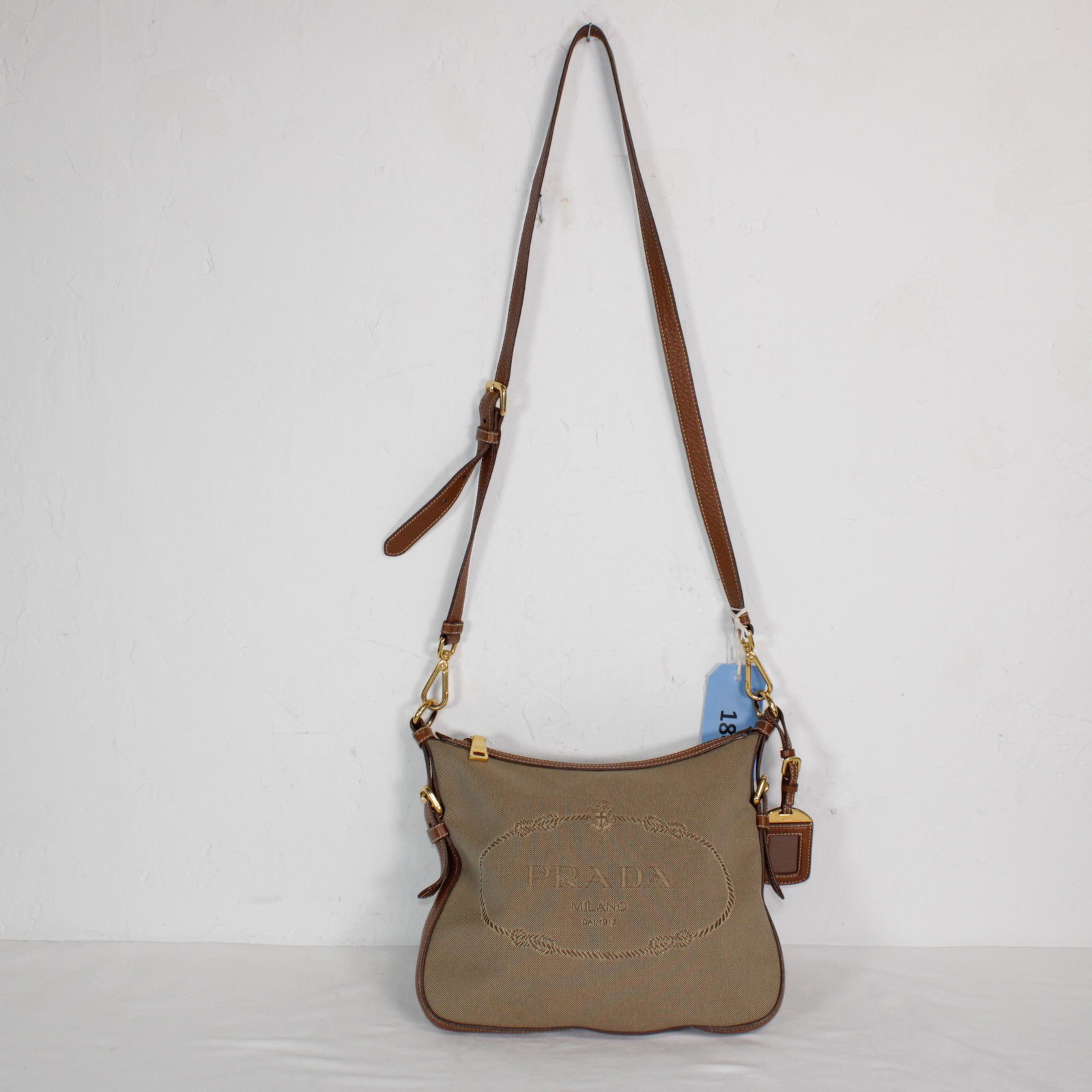 Prada Front Logo Crossbody Zip Tote in Canvas: Genuine Pre-Owned Prada Front Logo Crossbody Zip Tote in Khaki Green Canvas in AB condition. Date Code is N/A This lot includes Luggage Tag. Measurements: 27*23*2cm (Length * Height * Width). This lot