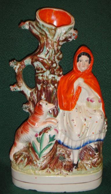 19th C. Staffordshire of Little Red Riding Hood: "Little Red Riding Hood." She is seated on a tree trunk, with an orange cloak and floral spring dress, with the reddish wolf creeping towards her. The tree has floral outcroppings. Oval with gilt trim
