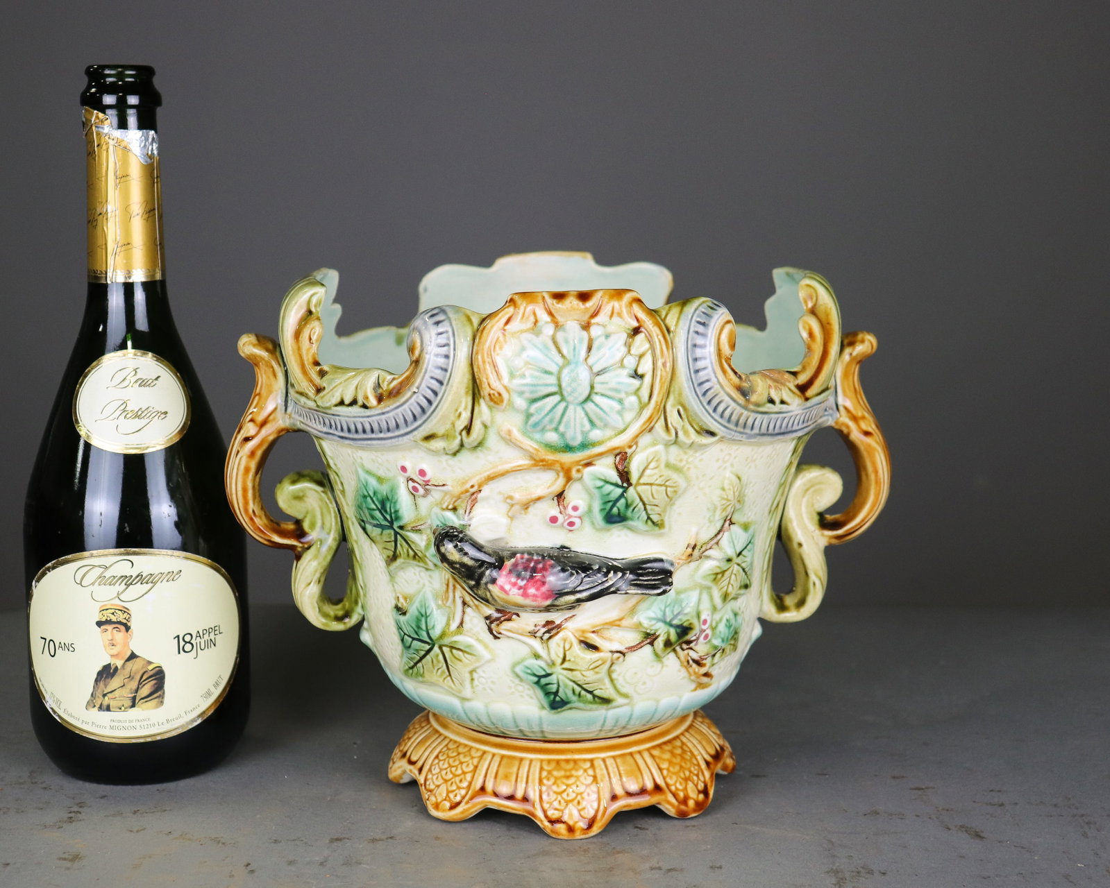 French Onnaing Style Majolica Bird & Floral Jardiniere: French Onnaing style majolica jardiniere featuring raised bird, floral and foliate decoration with ornate scrolling handles and a shaped footed base. Colorful glazed finish in green, amber and cream t