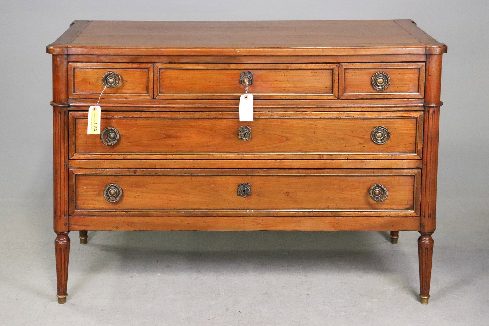 French Louis XVI Style Walnut Four Drawer Commode: French Louis XVI style walnut commode featuring a rectangular top above three smaller upper drawers and two wide lower drawers, paneled drawer fronts with brass ring pulls and escutcheons, fluted corn