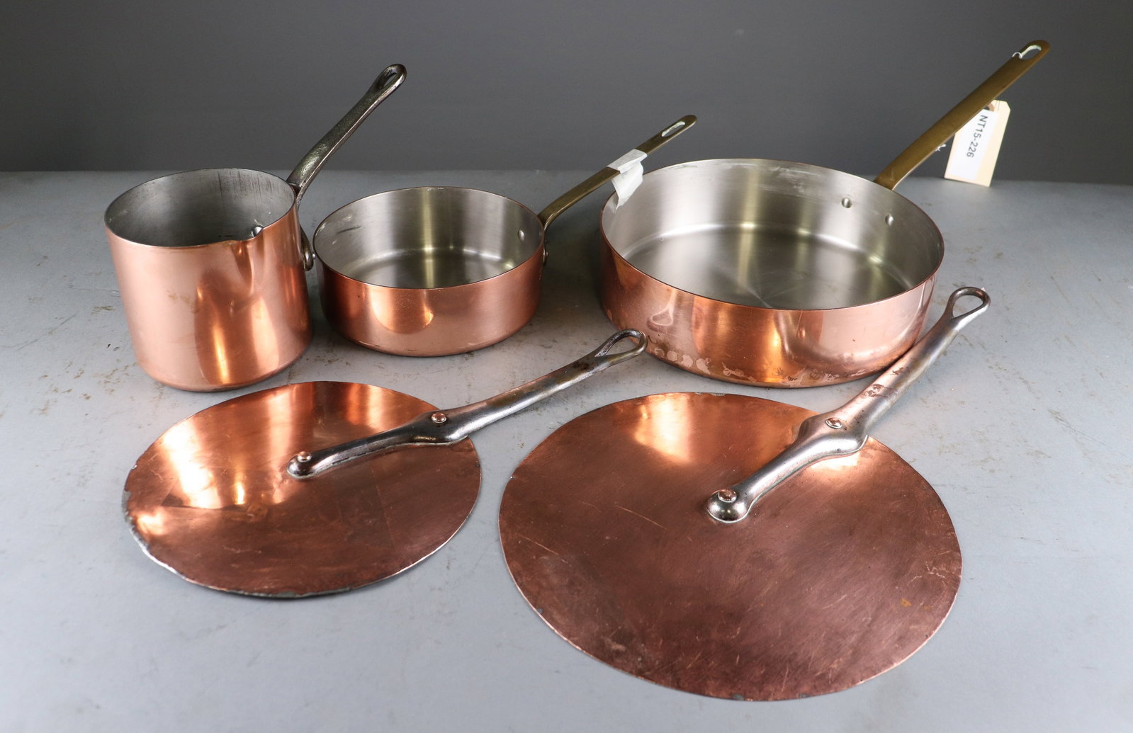 Group of French Copper Cookware & Pot Lids: Group of French copper cookware including three graduated saucepans with long riveted metal handles and two large handled copper lids. Interiors retain traditional tin lining. largest is 2.5 in tall x