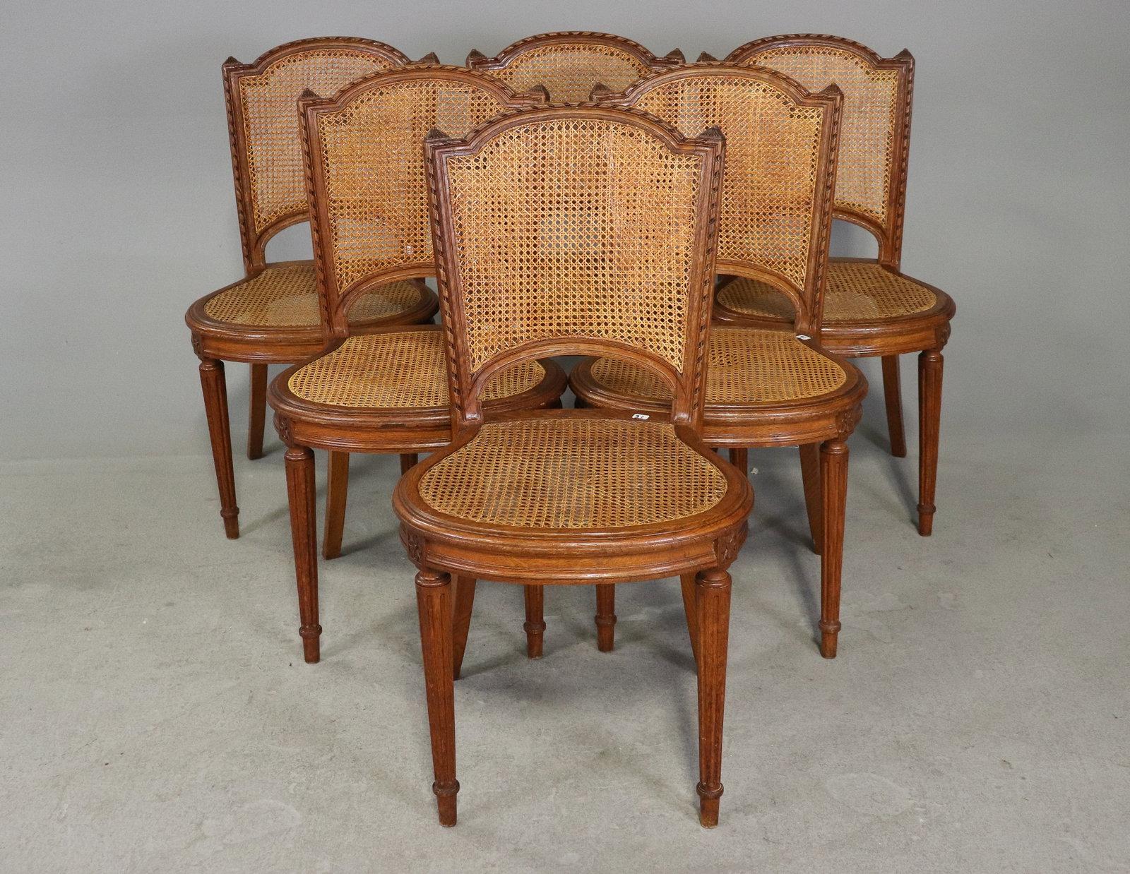 Set of 6 French Louis XVI Style Cane Dining Chairs: Set of six French Louis XVI style dining chairs with shaped cane backs and cane seats. Carved wood frames feature molded details, decorative crests and tapered fluted legs. Elegant French dining or oc