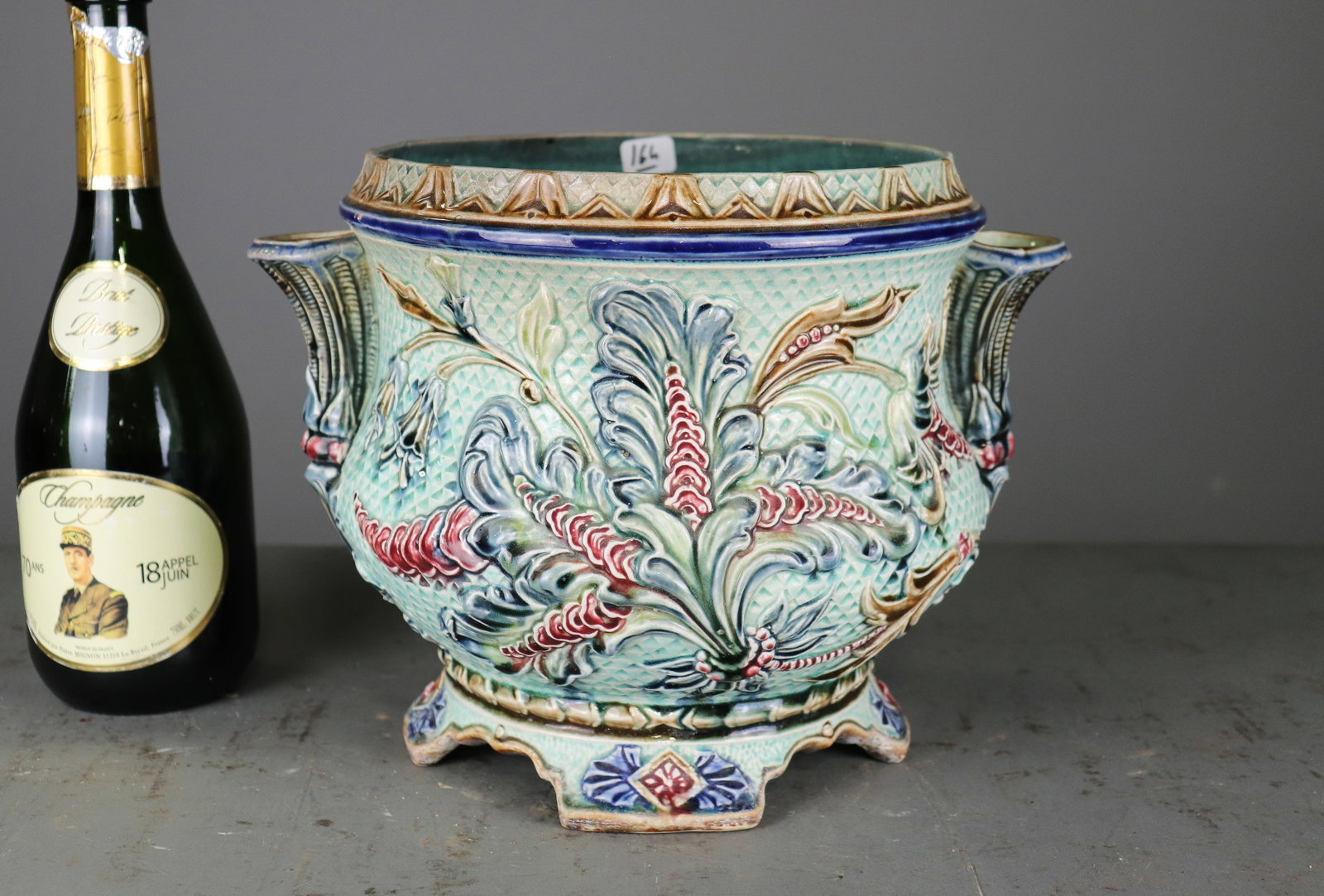 Majolica Turquoise Jardiniere with Floral Relief: Decorative majolica jardiniere with turquoise ground, elaborate molded floral and foliate relief, polychrome glazes, and sculptural side handles. Raised on an ornate shaped foot. 9 in tall x 12.5 x 10