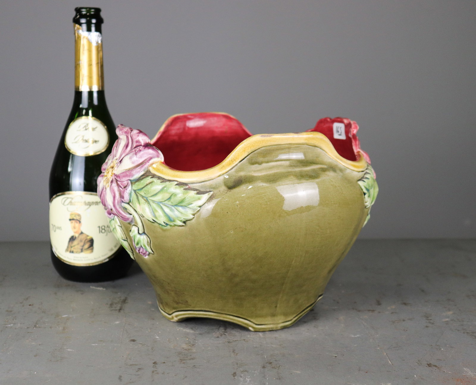 Marked Majolica Floral Jardiniere with Raised Flowers: Decorative majolica jardiniere with olive green ground, deep red interior, raised pink floral and green leaf decoration, and shaped rim. Impressed CAD mark to underside. 7.5 in tall x 11 x 10