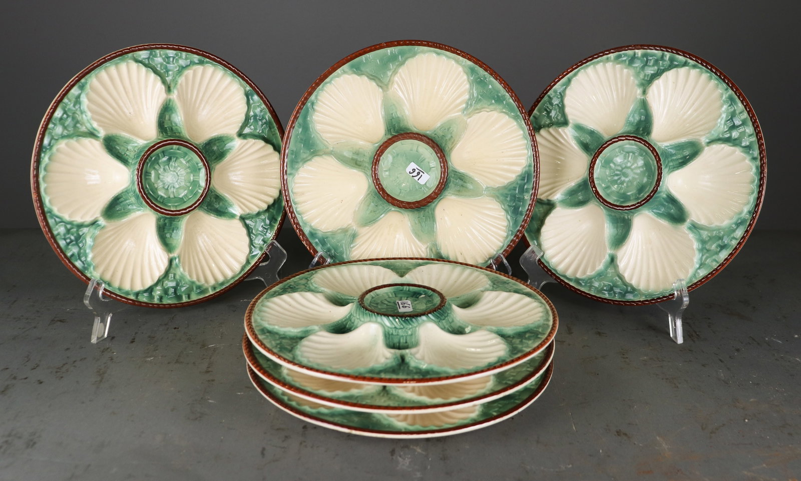 Set of 6 French Majolica Scallop Shell Plates: Set of six glazed majolica scallop / oyster plates, each molded with six cream colored scallop shells surrounding a raised center well. Green textured ground with brown border. Unmarked. 1 in x 9.5