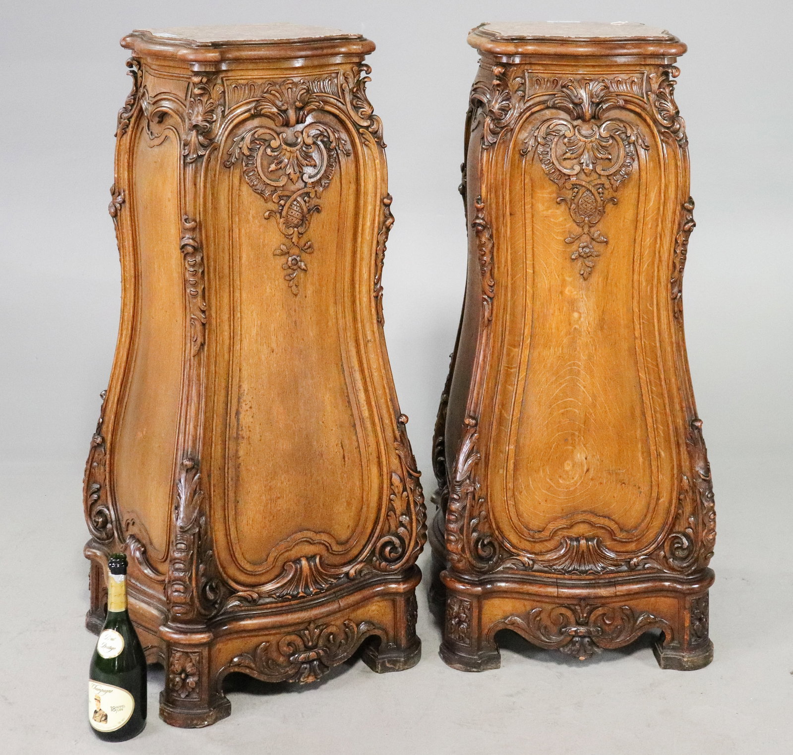 2 Antique French Louis XV Style Carved Walnut Marble Top Pedestals: 2 Antique French Louis XV style bombe carved walnut pedestals, each featuring a shaped inset marble top. Extensively decorated with carved rocaille, scroll and foliate motifs, with shaped paneled side