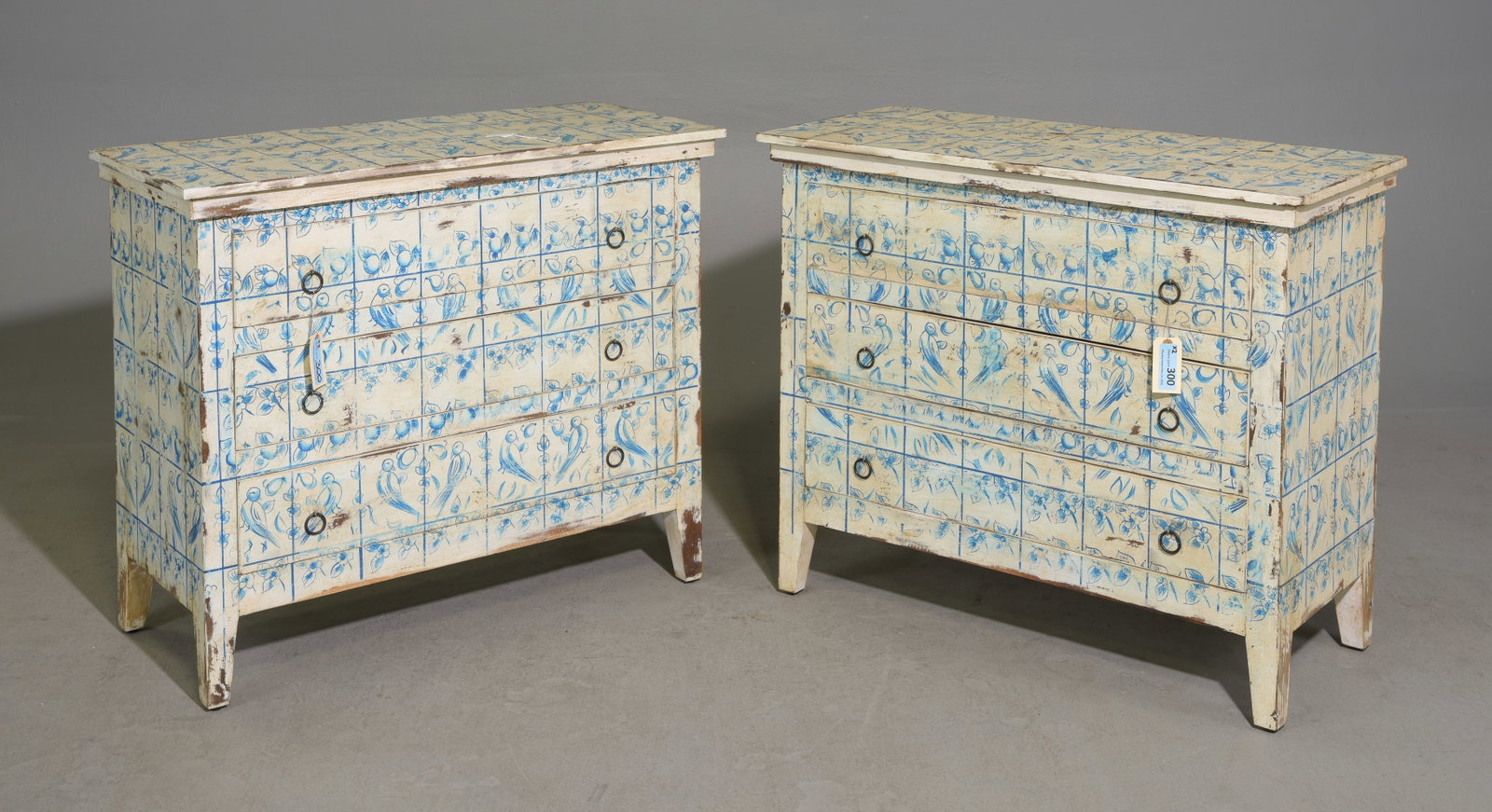 Pair Hand-Painted European Style Three Drawer Chests: Pair of European style three-drawer chests with hand-painted blue birds, fruit & foliate motif over cream background. The repeating dimensional motif covers the tops, fronts and sides with delicate