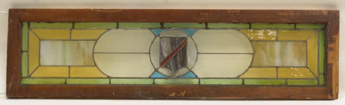 Antique Stained & Slag Glass Transom: Nice antique stained & slag glass transon with a shield in the center. Has a few cracks in the green border and has a wood frame with some damage. Measures 52" across x 14" tall.