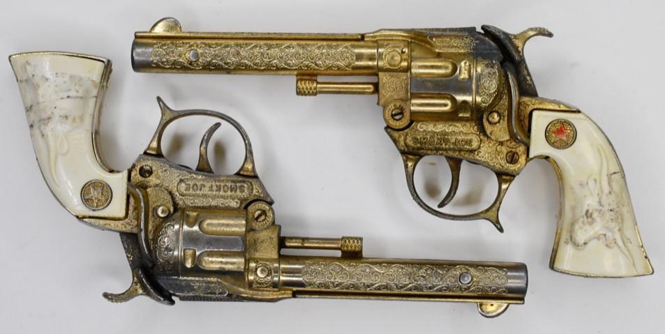 (2) Hubley Smoky Joe Cap Gun Pistols: Pair of Hubley Smoky Joe cap gun pistols. Both have tape holing the grips on. Both have corrosion and wear from play and age. Displays nicely with a gold finish. Measures approximately 7 3/4" long.