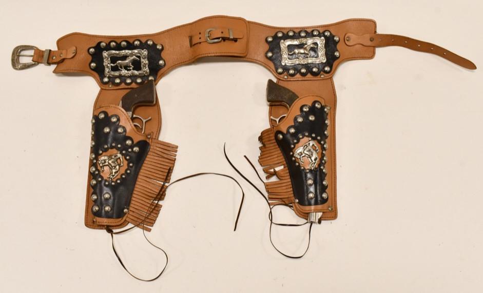 George Schmidt Range Rider Cap Guns w/ Holster: George Schmidt Range Rider cap gun set with leather holster. The trigger works on one gun, but the other one does not work. Displays well with some corrosion and wear from use and age. Comes with a fa