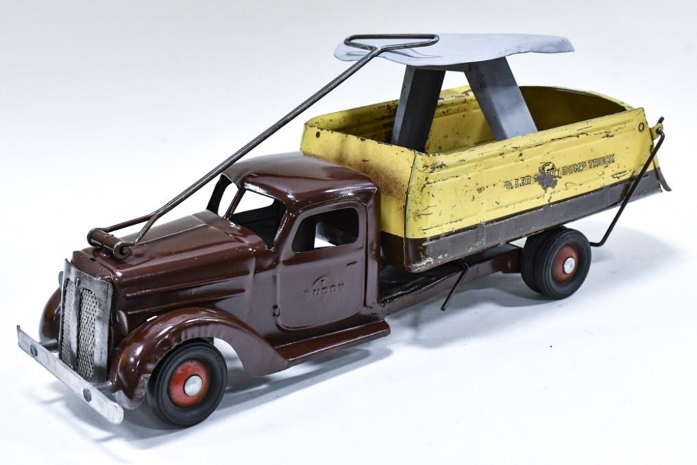 Buddy L Deluxe Rider Dump Truck: Buddy L Deluxe Rider Dump Truck. The truck displays well steering handle, rider seat, and dump bed with opening tailgate. The grill has been replaced. Measures approximately 22-1/2" long.