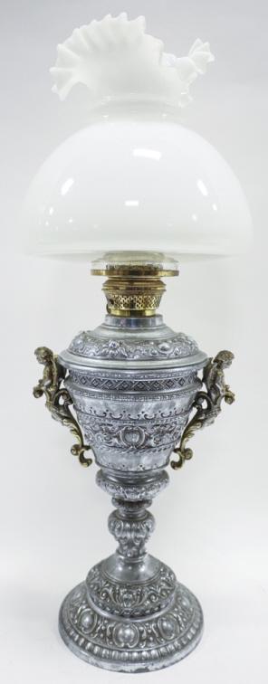 Victorian Cast Metal Kerosene Parlor Lamp: Victorian cast metal kerosene parlor lamp with ruffled white glass shade. Urn form with figural double handles. Internal glass vessel has fracture. Measures 8" across, 24" tall.
